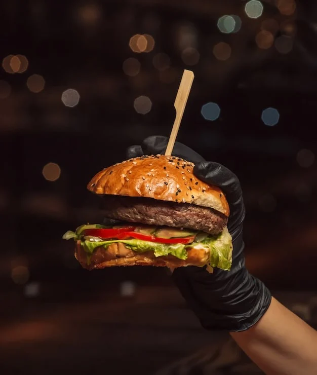 Ein Burger in einer Hand mit schwarzem Handschuh